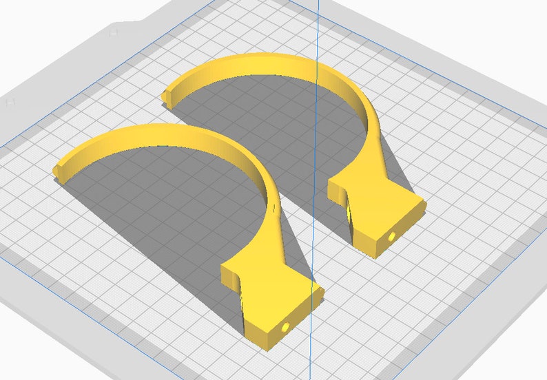 May include: Two yellow, semi-circular objects with a flat base and a small hole. The objects are on a grid background, casting shadows. The design appears to be a 3D rendering or a digital model.