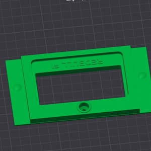 May include: A bright green rectangular plastic component with the text "REDBULL E" embossed on the top. The component has a rectangular cutout in the center and a circular hole at the bottom. Two small circular protrusions are on the sides.