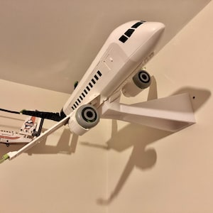May include: A white airplane model mounted on a white wall mount. The airplane has black accents and a black tail. The model is mounted on a white wall mount.