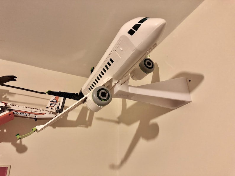 May include: A white airplane model mounted on a white wall mount. The airplane has black accents and a black tail. The model is mounted on a white wall mount.