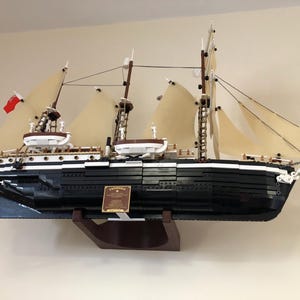 May include: A black and white LEGO model of a ship with sails, a wooden base, and a plaque that reads "Lady Washington."