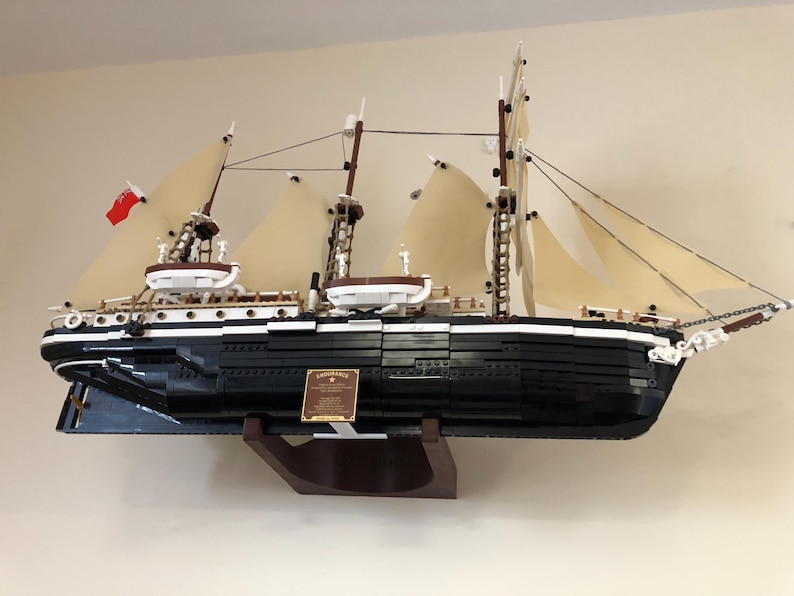 May include: A black and white LEGO model of a ship with sails, a wooden base, and a plaque that reads "Lady Washington."