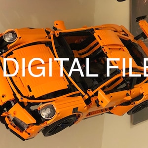 May include: An orange Lego Porsche 911 GT3 RS model car with black accents and a rear wing. The car is suspended in mid-air and the text "DIGITAL FILE" is superimposed on the image.