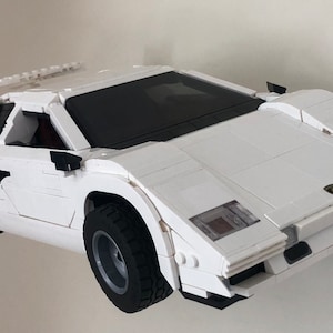 May include: A white Lego model of a Lamborghini Countach sports car with black accents and a rear wing. The car is built with Lego bricks and has a detailed interior.