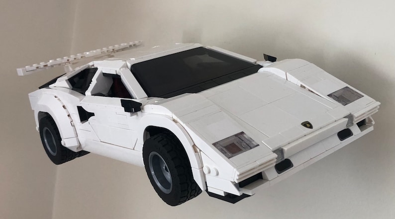 May include: A white Lego model of a Lamborghini Countach sports car with black accents and a rear wing. The car is built with Lego bricks and has a detailed interior.