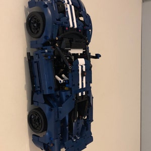May include: A blue Lego model of a Ford GT race car with white racing stripes. The car is displayed on a wall with the wheels facing out.