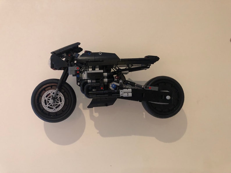 May include: A black Lego motorcycle model with detailed engine and wheels. The motorcycle is mounted on a white wall.