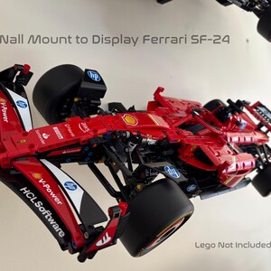 May include: A red, black, and white Lego Ferrari SF-24 race car model mounted on a wall display stand. The car has sponsors' logos including V-Power, HCL Software, and AWS.