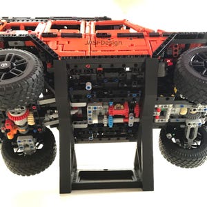 May include: A black and orange Lego model of a Mercedes-Benz G-Wagon on a black display stand. The model is upside down, showing the underside of the vehicle.