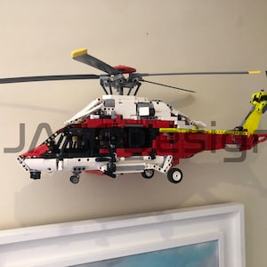 May include: A red, white, and black Lego helicopter model with a yellow tail rotor. The helicopter is mounted on a wall.