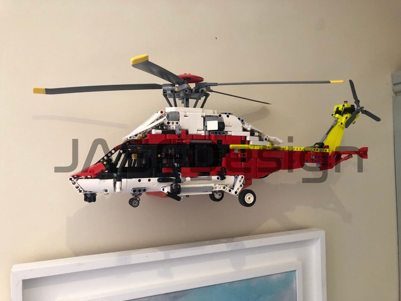May include: A red, white, and black Lego helicopter model with a yellow tail rotor. The helicopter is mounted on a wall.