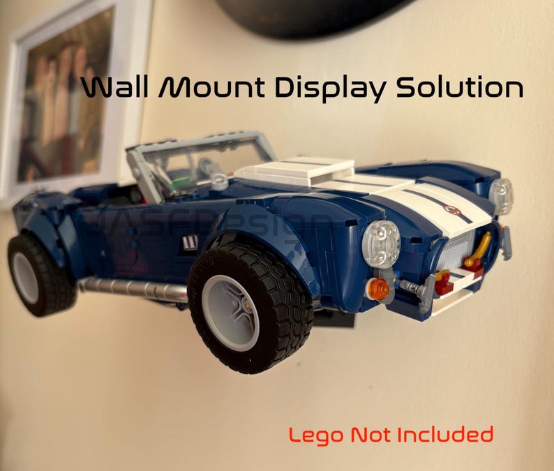 Op de afbeelding: Een blauwe en witte speelgoedauto aan de muur gemonteerd. De auto heeft zwarte banden en een witte streep in het midden. Tekst op de afbeelding luidt "Wall Mount Display Solution" en "Lego Not Included".