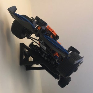 May include: A black and blue race car model mounted on a black wall mount. The car is angled upwards and has orange accents.