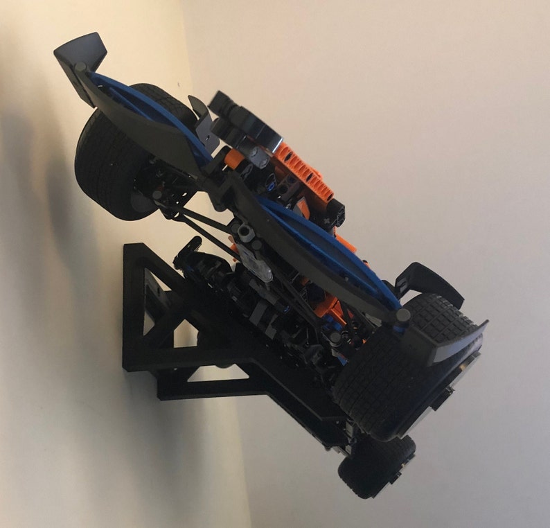 May include: A black and blue race car model mounted on a black wall mount. The car is angled upwards and has orange accents.