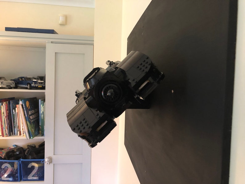 K&ouml;nnte beinhalten: Ein schwarzes Lego Batmobil-Modell, das auf einem schwarzen Pr&auml;sentationsst&auml;nder montiert ist. Das Batmobil ist leicht nach rechts geneigt und die Vorderr&auml;der sind sichtbar.