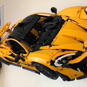 May include: A yellow and black Lego McLaren Senna model car with detailed features, including a black engine and white headlights. The car is mounted on a wall.