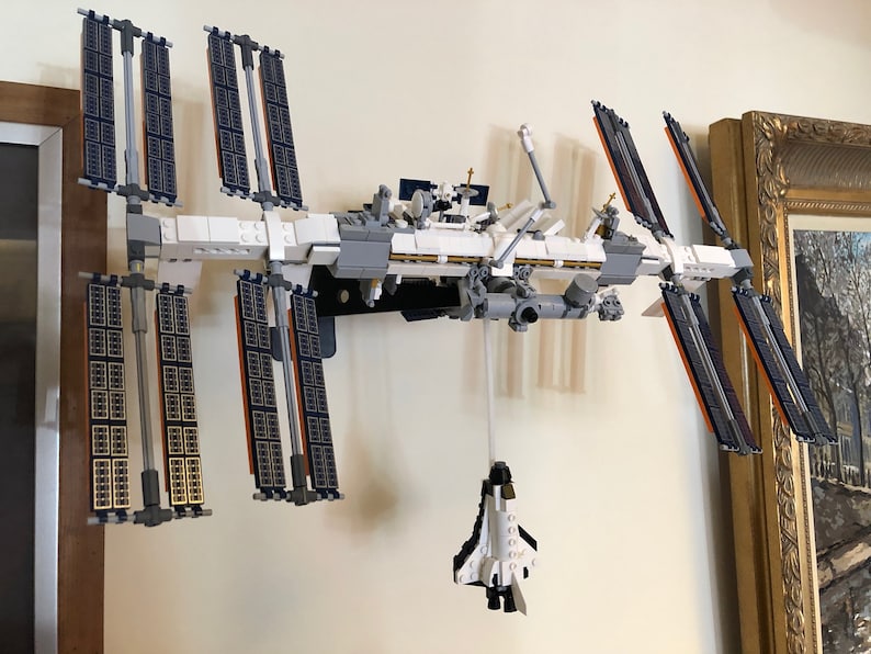 May include: A white and gray Lego model of the International Space Station with solar panels and a space shuttle attached.