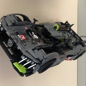 May include: A gray and green race car model with the number 66 and the text "TE" on the side. The car has a detailed engine and a spoiler.