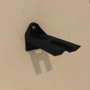 May include: A black plastic wall mount with a single screw. The mount has two prongs extending out from the side.