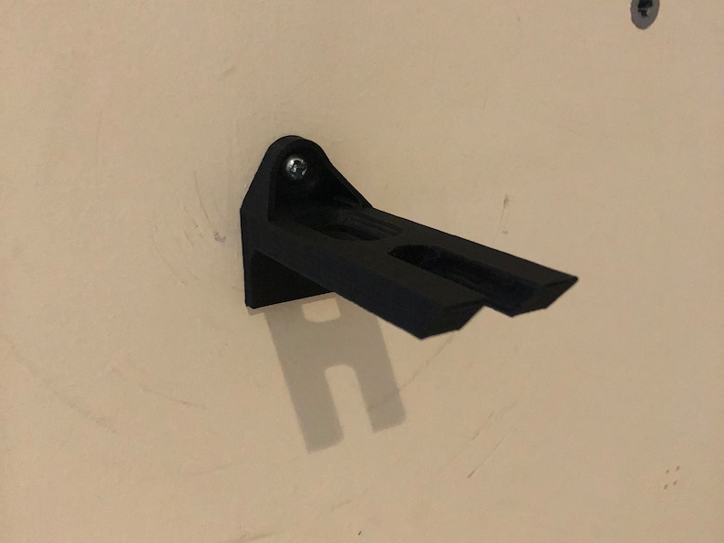 May include: A black plastic wall mount with a single screw. The mount has two prongs extending out from the side.