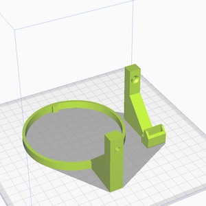 May include: A 3D printed green plastic holder for a circular object, such as a fan or a speaker. The holder has a base and a ring that can be adjusted to fit different sizes.
