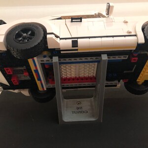 May include: A white Lego Porsche 911 Turbo model car on a gray stand with the text "911 Turbo" printed on the stand.