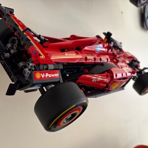May include: A red and black Lego Ferrari Formula 1 race car model with the V-Power logo and the text "Ray-Ban" on the side. The car is mounted on a wall.