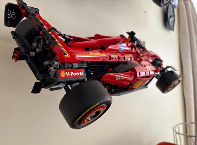 May include: A red and black Lego Ferrari Formula 1 race car model with the V-Power logo and the text "Ray-Ban" on the side. The car is mounted on a wall.