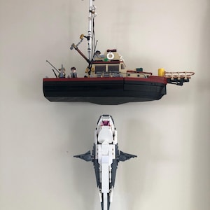 May include: A Lego model of a fishing boat with a black hull, red trim, and a white cabin. Below it is a Lego model of a shark, white on the belly and gray on the back. The boat has a mast and various details.