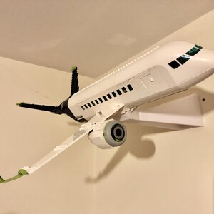 May include: A white airplane model with green and black accents is mounted on a white wall shelf. The airplane has a single engine and a detailed cockpit.
