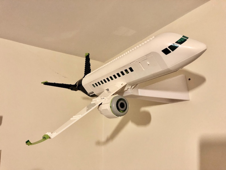 May include: A white airplane model with green and black accents is mounted on a white wall shelf. The airplane has a single engine and a detailed cockpit.