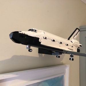 May include: A white and black model of a space shuttle, mounted on a wall. The model has the words "United States" printed on the side. The shuttle is displayed above a framed picture.