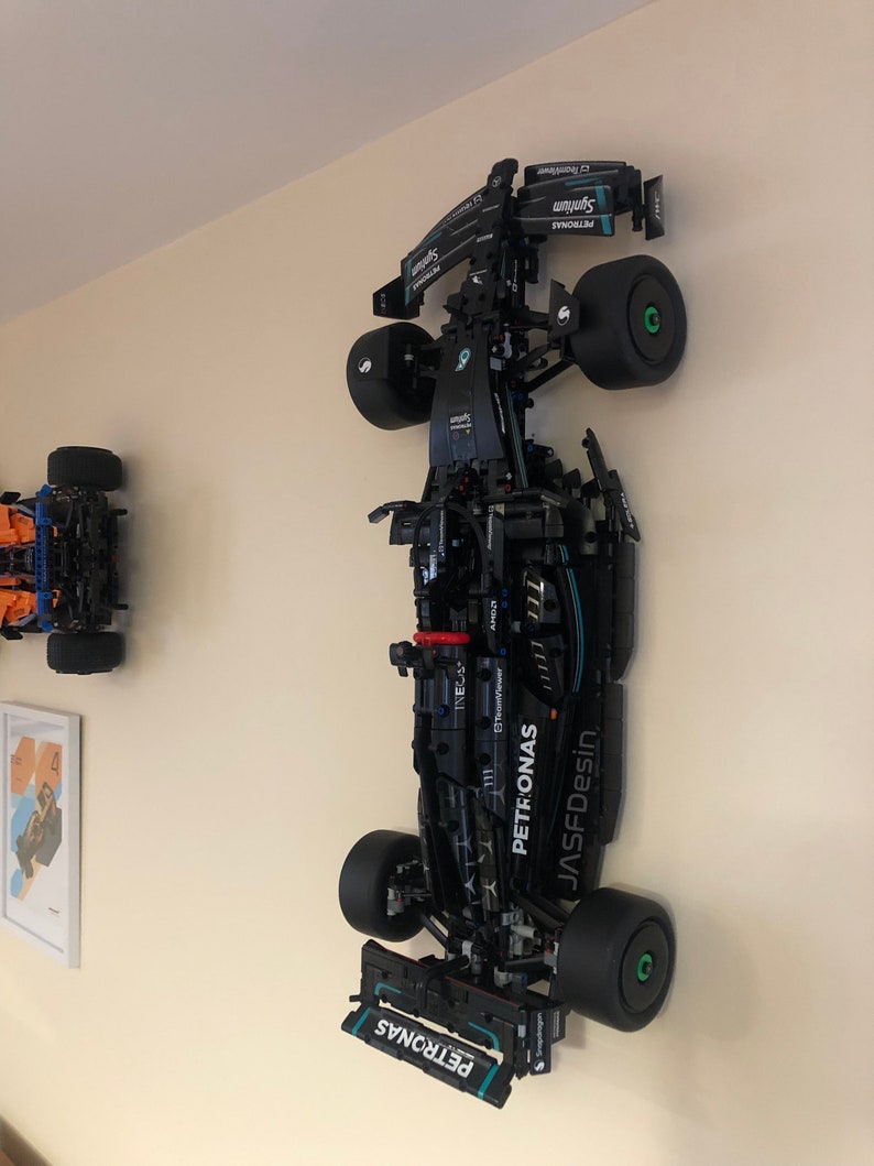 May include: A black and green Lego model of a Formula 1 race car with the Petronas logo on the side. The car is mounted on a wall.