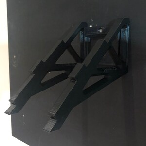 May include: A black wall-mounted stand made of plastic with a geometric design. The stand is designed to hold a laptop or tablet.