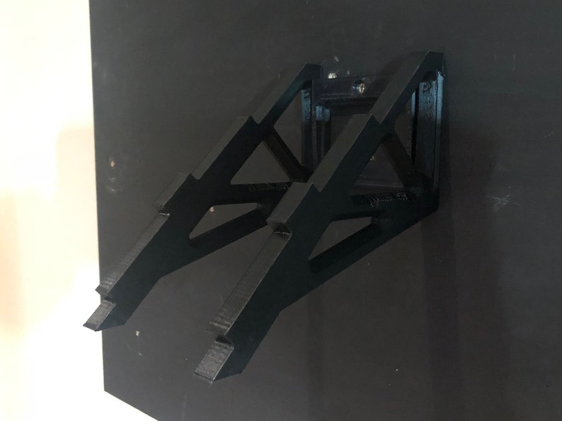 May include: A black wall-mounted stand made of plastic with a geometric design. The stand is designed to hold a laptop or tablet.