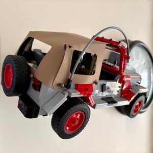 May include: A building block model of a red and gray off-road vehicle featuring a tan fabric roof, a spare tire mounted on the rear, black treaded tires with red rims, and a curved gray roll bar structure extending over the open cabin area.