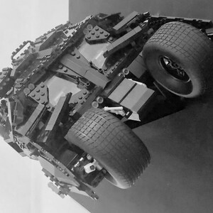 May include: A black Lego model of the Batmobile from the Batman movie franchise. The model is detailed with black Lego bricks and features a black tire with a tread pattern.