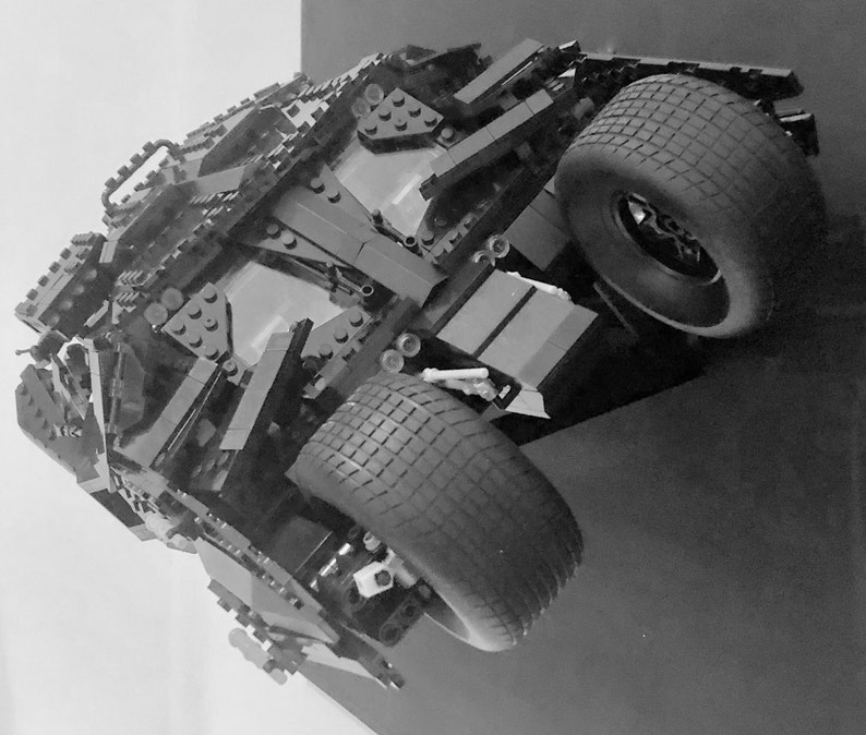May include: A black Lego model of the Batmobile from the Batman movie franchise. The model is detailed with black Lego bricks and features a black tire with a tread pattern.