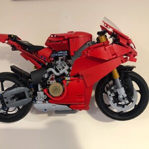 May include: A red and black Lego motorcycle model with a detailed engine and a clear windshield. The motorcycle has a black front tire and a black rear tire.