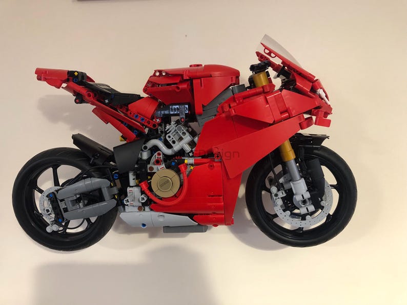 May include: A red and black Lego motorcycle model with a detailed engine and a clear windshield. The motorcycle has a black front tire and a black rear tire.