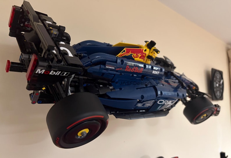 May include: A blue and black Lego model of a Formula One race car with the Red Bull logo and Mobil 1 sponsorship. The car is mounted on a wall and has a yellow and red spoiler.