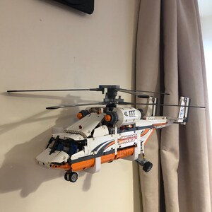 May include: A white and orange Lego helicopter model with a black and gray rotor, mounted on a wall. The helicopter has the words "Heavy Lift Service" printed on the side.