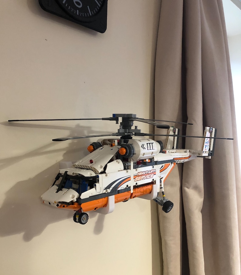 May include: A white and orange Lego helicopter model with a black and gray rotor, mounted on a wall. The helicopter has the words "Heavy Lift Service" printed on the side.