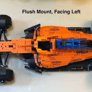 May include: A black and orange Lego Formula 1 race car with the words "WOMW" and "webex" printed on the side. The car is facing left and is mounted flush to the surface.