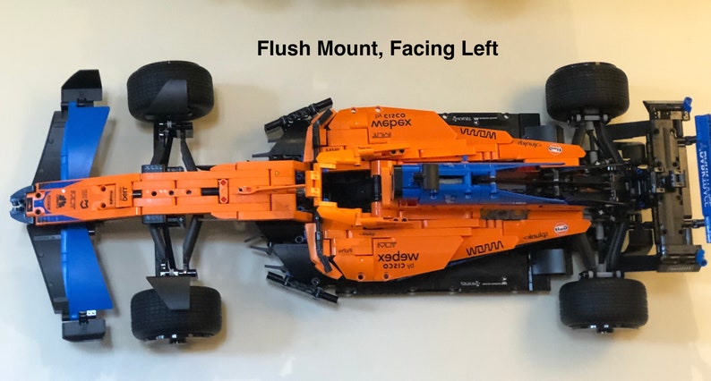 May include: A black and orange Lego Formula 1 race car with the words "WOMW" and "webex" printed on the side. The car is facing left and is mounted flush to the surface.
