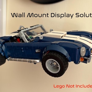 Op de afbeelding: Een blauwe en witte speelgoedauto aan de muur gemonteerd. De auto heeft een klassiek ontwerp met witte racestrepen. De tekst "Wall Mount Display Solution" staat boven de auto en "Lego Not Included" staat eronder.
