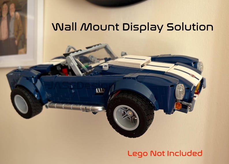 Op de afbeelding: Een blauwe en witte speelgoedauto aan de muur gemonteerd. De auto heeft een klassiek ontwerp met witte racestrepen. De tekst "Wall Mount Display Solution" staat boven de auto en "Lego Not Included" staat eronder.