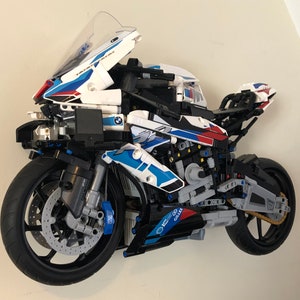 May include: A white, blue, and red LEGO&reg; Technic&trade; BMW M 1000 RR motorcycle model with a black frame and gold chain. The motorcycle has a clear windshield and a detailed engine.