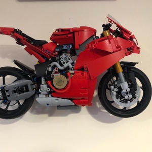 May include: A red and black Lego motorcycle model with a detailed engine and wheels. The motorcycle is built with Lego bricks and is a replica of a real motorcycle.