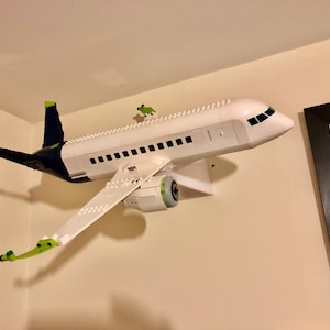 May include: A white and blue Lego airplane model mounted on a wall. The airplane has green accents and a detailed cockpit.